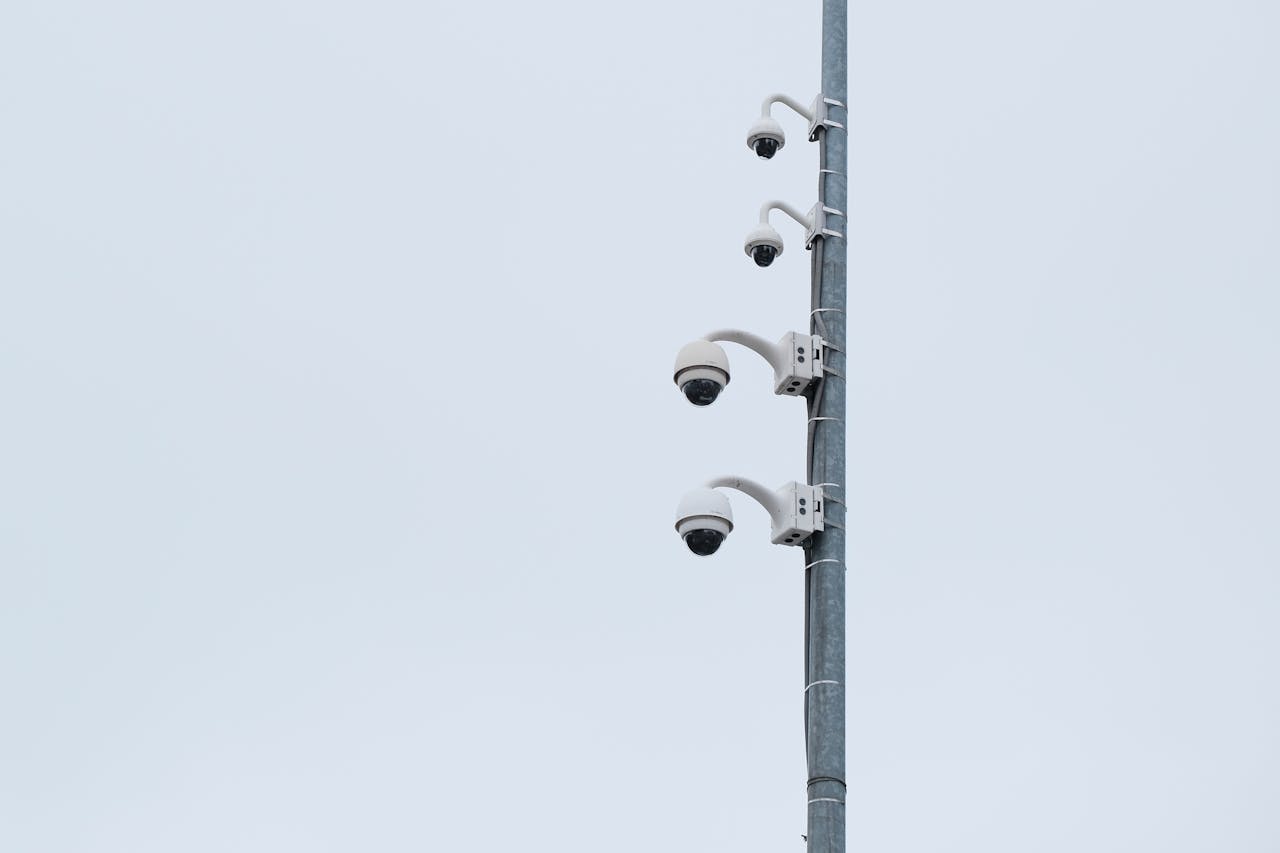 A collection of security cameras mounted on a tall pole against a cloudy sky, capturing urban safety.